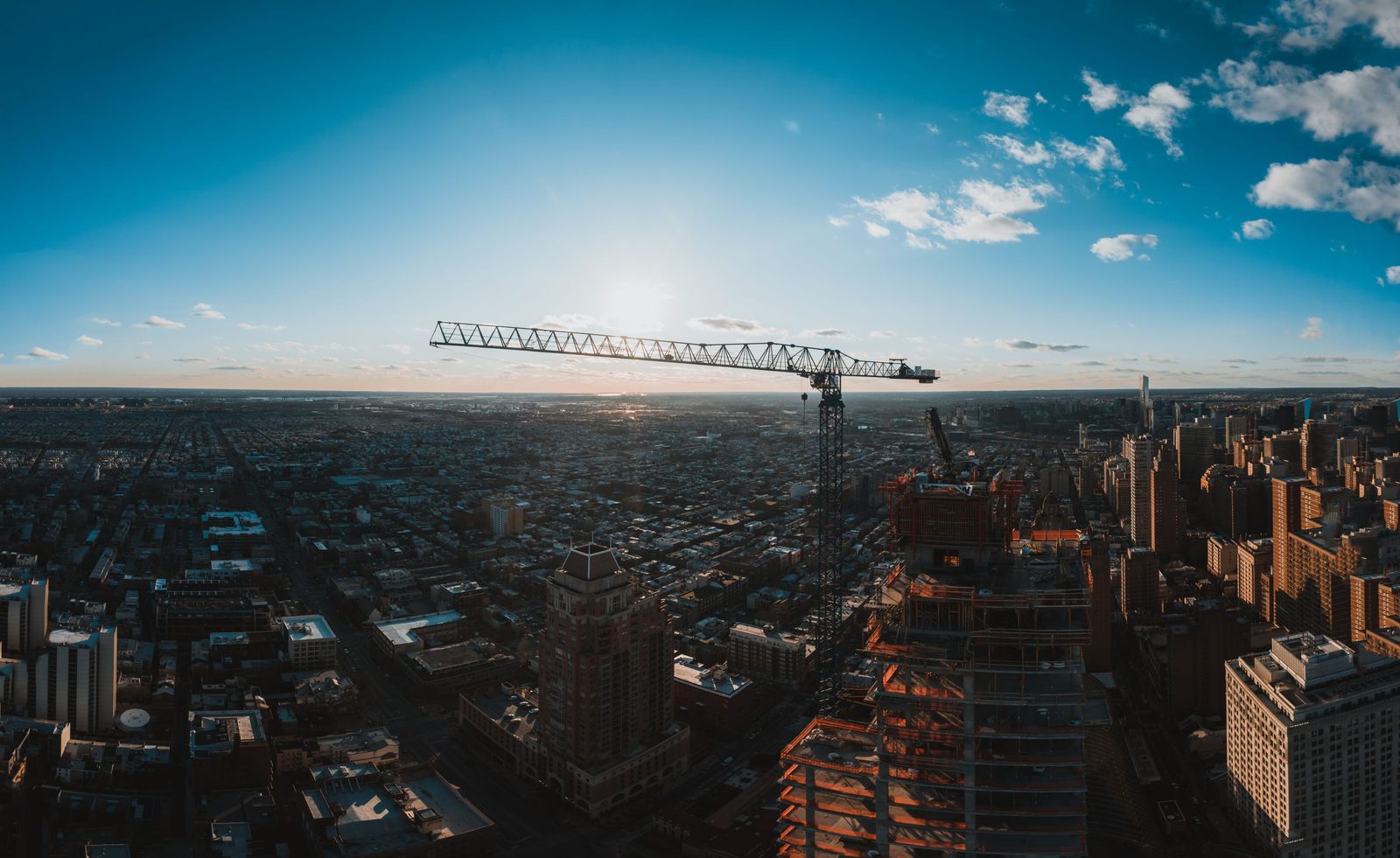 Guindaste de uma obra sobre a cidade vista do alto, com céu azul